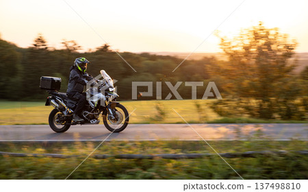 Driver riding motorcycle on empty road during sunset, spring mountains Driver riding motorcycle on empty road during sunset, spring mountains 137498810