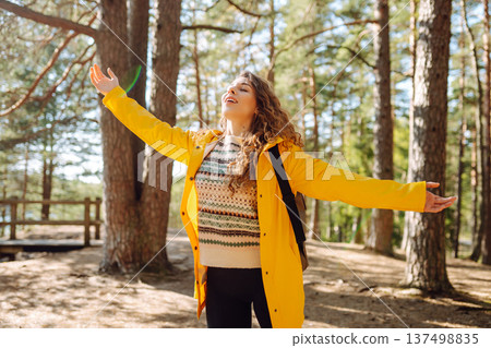 A cheerful young woman in a yellow jacket enjoying a sunny day by the lake. Trips. Active lifestyle. 137498835