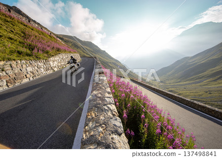 Motorcycle rider riding in Italian Alps during sunrise, dramatic sky. Travel and freedom, outdoor activities Motorcycle rider riding in Italian Alps during sunrise, dramatic sky. Travel and freedom, outdoor activities 137498841
