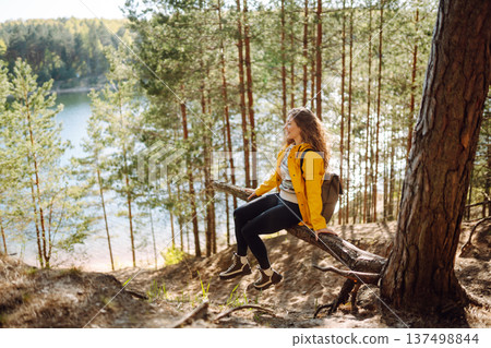 A cheerful young woman in a yellow jacket enjoying a sunny day by the lake. Trips. Active lifestyle. A cheerful young woman in a yellow jacket enjoying a sunny day by the lake. Trips. Active lifestyle. 137498844