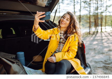Happy Woman is resting in trunk of car and taking selfie. Travel, tourism, nature, active life. Happy Woman is resting in trunk of car and taking selfie. Travel, tourism, nature, active life. 137498845