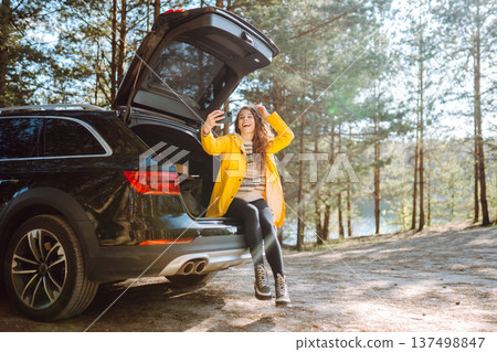 Happy Woman is resting in trunk of car and taking selfie. Travel, tourism, nature, active life. Happy Woman is resting in trunk of car and taking selfie. Travel, tourism, nature, active life. 137498847