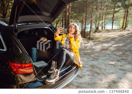 Happy Woman is resting in trunk of car and taking selfie. Travel, tourism, nature, active life. Happy Woman is resting in trunk of car and taking selfie. Travel, tourism, nature, active life. 137498848