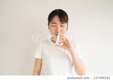 Asian woman using nasal spray suspension for relieve symptoms such as sneezing, runny or itchy nose. Medical device used to treat allergic rhinitis, hay fever, sinusitis or nasal polyps. Asian woman using nasal spray suspension for relieve symptoms such as sneezing, runny or itchy nose. Medical device used to treat allergic rhinitis, hay fever, sinusitis or nasal polyps. 137499392