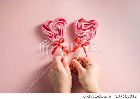 Valentine's Day festive background. Female hand holding heart-shaped lollipops on grey background with copy space. Love concept Valentine's Day festive background. Female hand holding heart-shaped lollipops on grey background with copy space. Love concept 137500032