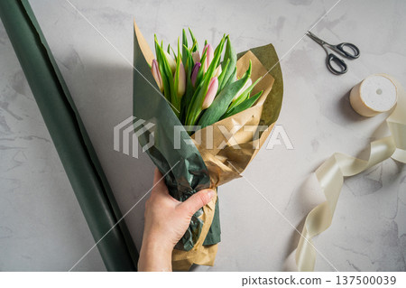 Mother's day, birthday bouquet. Female hands wrapping tulip flowers in craft paper. Spring tulips flower background Mother's day, birthday bouquet. Female hands wrapping tulip flowers in craft paper. Spring tulips flower background 137500039