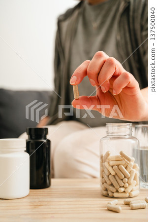 Food supplements and vitamins. Woman holding a pill capsule with pill bottles at home, healthy care concept. 137500040