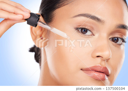 Woman, portrait and oil serum for beauty, cosmetics and skincare product on a blue background. Young person with facial liquid, dermatology dropper or collagen for skin care makeup on face in studio Woman, portrait and oil serum for beauty, cosmetics and skincare product on a blue background. Young person with facial liquid, dermatology dropper or collagen for skin care makeup on face in studio 137500104