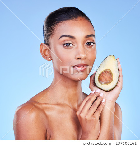 Avocado, beauty and portrait of woman in studio for cosmetics, nutrition and diet on blue background. Indian model, skincare and fruit for sustainable dermatology, vegan wellness and facial benefits 137500161