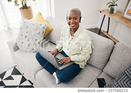 Portrait of black woman, remote work or laptop on sofa in living room for online research in headphones. Happy, top view or journalist working on computer for streaming or social media blog at home Portrait of black woman, remote work or laptop on sofa in living room for online research in headphones. Happy, top view or journalist working on computer for streaming or social media blog at home 137500233