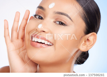 Portrait, beauty and woman with cream, skincare and dermatology on blue studio background. Face, person and model with beauty, lotion or wellness with shine, smile or glow with aesthetic or creme Portrait, beauty and woman with cream, skincare and dermatology on blue studio background. Face, person and model with beauty, lotion or wellness with shine, smile or glow with aesthetic or creme 137500281