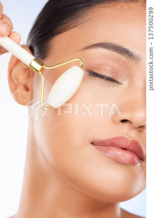 Woman, face roller and massage in studio for skincare, grooming and aesthetic dermatology on white background. Model, crystal cosmetics and facial beauty tools for lymphatic drainage, shine and glow 137500299