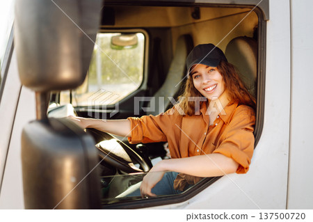 Portrait of beautiful young woman professional truck driver driving a big truck. Inside of vehicle Portrait of beautiful young woman professional truck driver driving a big truck. Inside of vehicle 137500720