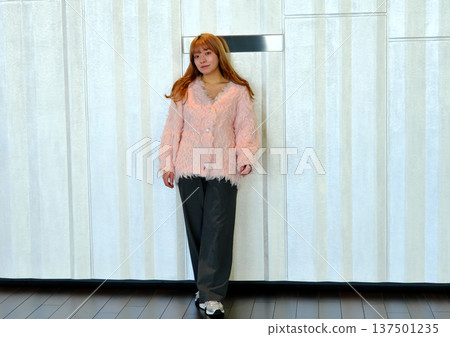 A female model posing in a modern space. A feminine indoor portrait featuring a pink knit. A female model posing in a modern space. A feminine indoor portrait featuring a pink knit. 137501235
