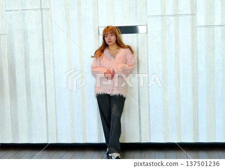 A female model posing in a modern space. A feminine indoor portrait featuring a pink knit. 137501236