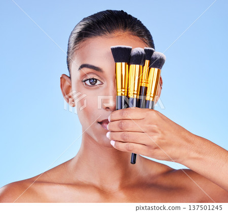 Woman, portrait and beauty, makeup brush on eye, foundation with cosmetics isolated on blue background, Indian model face, wellness and cosmetology with tools or equipment, skin and shine in studio Woman, portrait and beauty, makeup brush on eye, foundation with cosmetics isolated on blue background, Indian model face, wellness and cosmetology with tools or equipment, skin and shine in studio 137501245