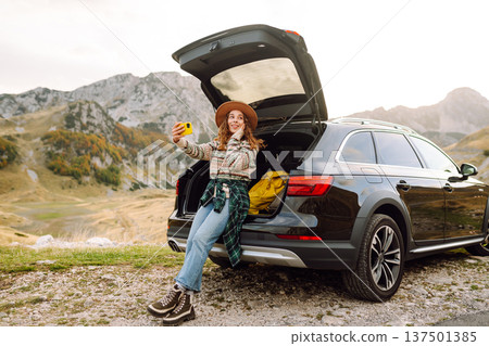 Young traveler woman taking a selfie by her car in the mountains during sunset. Lifestyle, travel 137501385