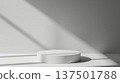 A simple white cylindrical pedestal is illuminated by natural sunlight, casting geometric shadows on a plain background. 137501788