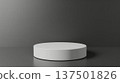 A minimalist round white pedestal is placed in front of a dark gray backdrop under soft studio lighting, creating a clean and modern presentation. 137501826