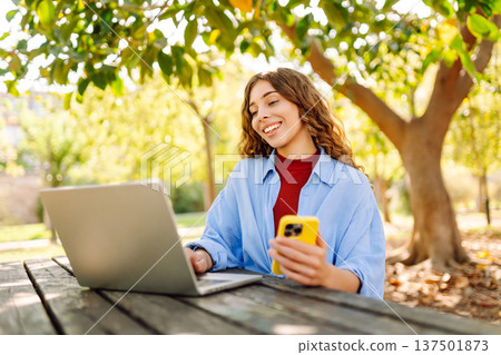 Happy woman with laptop and phone at table in an outdoor near lake. Business, blogging, freelancing. Happy woman with laptop and phone at table in an outdoor near lake. Business, blogging, freelancing. 137501873