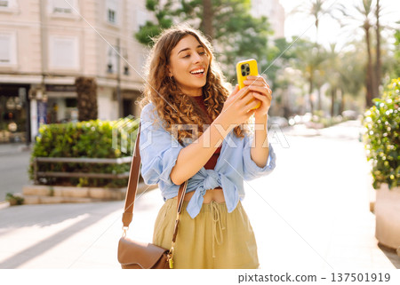 Smiling woman walking around old street using smartphone. Communication, social networks concept. Smiling woman walking around old street using smartphone. Communication, social networks concept. 137501919