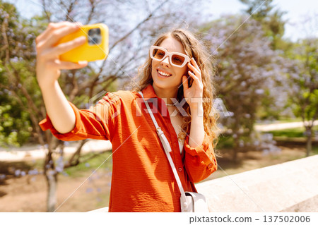 Young woman taking a cheerful selfie in blooming park on a sunny day. Joy concept. Active lifestyle. 137502006