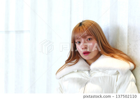 A female model leaning against a white wall. A sophisticated winter indoor portrait with a clean white outerwear. A female model leaning against a white wall. A sophisticated winter indoor portrait with a clean white outerwear. 137502110