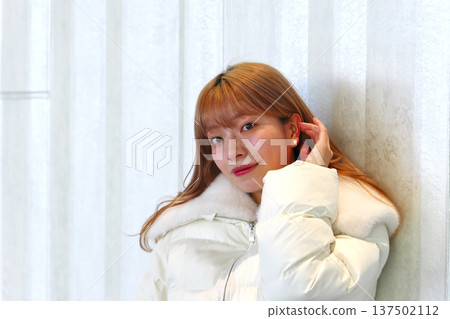 一位女模特兒倚靠在白牆上。這是一張精緻的冬季室內肖像照,她穿著乾淨的白色外套。 一位女模特兒倚靠在白牆上。這是一張精緻的冬季室內肖像照,她穿著乾淨的白色外套。 137502112