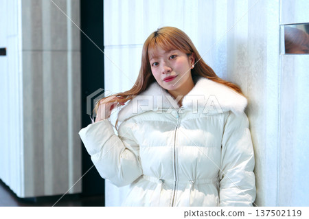 一位女模特兒倚靠在白牆上。這是一張精緻的冬季室內肖像照,她穿著乾淨的白色外套。 一位女模特兒倚靠在白牆上。這是一張精緻的冬季室內肖像照,她穿著乾淨的白色外套。 137502119