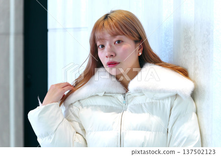 一位女模特兒倚靠在白牆上。這是一張精緻的冬季室內肖像照,她穿著乾淨的白色外套。 一位女模特兒倚靠在白牆上。這是一張精緻的冬季室內肖像照,她穿著乾淨的白色外套。 137502123