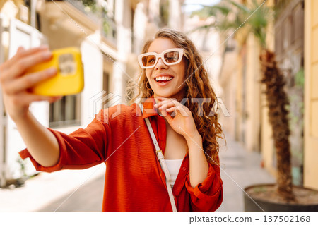 Cheerful woman taking a selfie in stylish sunglasses while strolling down a sunlit city street Cheerful woman taking a selfie in stylish sunglasses while strolling down a sunlit city street 137502168