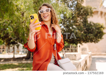 Cheerful woman taking a selfie in stylish sunglasses while strolling down a sunlit city street Cheerful woman taking a selfie in stylish sunglasses while strolling down a sunlit city street 137502169