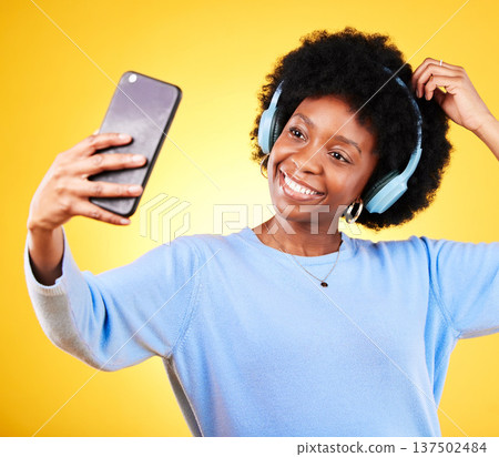 Happy black woman, phone and selfie with headphones for listening to music against a yellow studio background. African female person smile, afro or mobile smartphone app in photography or podcast 137502484