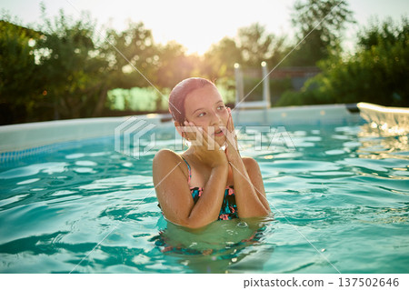 Girl enjoying a refreshing swim in a pool during a warm summer evening while the sun sets in the background Girl enjoying a refreshing swim in a pool during a warm summer evening while the sun sets in the background 137502646