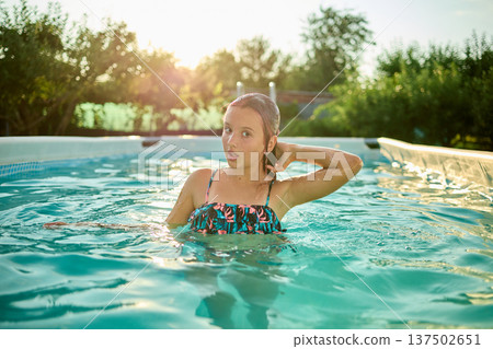 Girl enjoying a sunny summer day while swimming in a pool surrounded by greenery and sunlight in a charming backyard setting Girl enjoying a sunny summer day while swimming in a pool surrounded by greenery and sunlight in a charming backyard setting 137502651