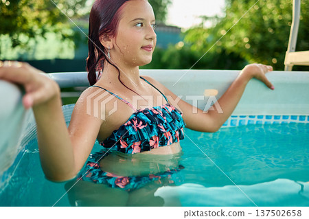 Teen girl enjoying a summer afternoon in a backyard pool surrounded by lush greenery and sunshine Teen girl enjoying a summer afternoon in a backyard pool surrounded by lush greenery and sunshine 137502658