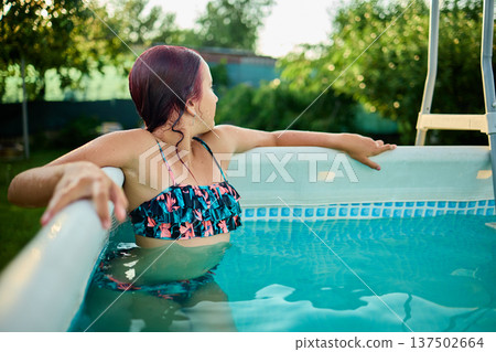 Teen girl enjoying a summer afternoon in a backyard pool surrounded by lush greenery and sunshine Teen girl enjoying a summer afternoon in a backyard pool surrounded by lush greenery and sunshine 137502664