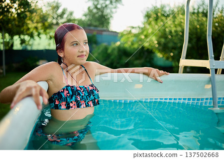 Teen girl enjoying a summer afternoon in a backyard pool surrounded by lush greenery and sunshine Teen girl enjoying a summer afternoon in a backyard pool surrounded by lush greenery and sunshine 137502668