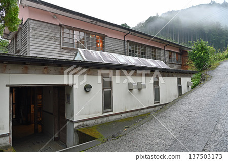 The rain-soaked exterior of a retro wooden school building quietly nestled in a misty mountain village 137503173