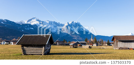 Traditional wooden hut in Bavarian countryside with snow capped Alps mountains and clear blue sky 137503370