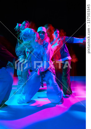 Hip hop dancers performing synchronized street dance under colorful neon lighting with motion blur 137503845
