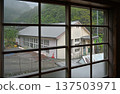 A wooden school gymnasium nestled in a misty mountain village seen through a window on a rainy day 137503971
