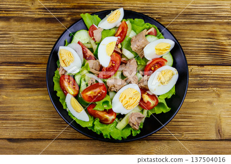 Tasty tuna salad with eggs, lettuce and fresh vegetables on wooden table. Top view 137504016