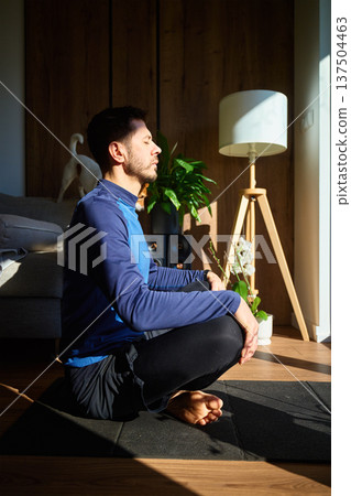 Man meditating on exercise mat in sunlight at home living room Man meditating on exercise mat in sunlight at home living room 137504463