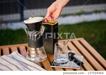 Specialty pour over coffee setup with hand placing paper filter outdoors 137504468