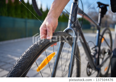 Hand checking bicycle tire for puncture on outdoor road 137504476