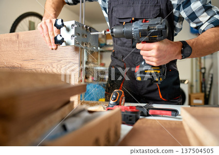 Carpenter drilling wooden board with cordless drill and drilling jig 137504505