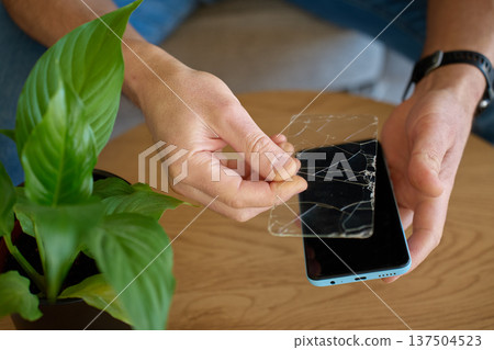 Man removing cracked protective glass from smartphone at home Man removing cracked protective glass from smartphone at home 137504523