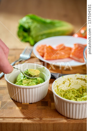 Hand mashing avocado in ramekin on cutting board with salmon Hand mashing avocado in ramekin on cutting board with salmon 137504581