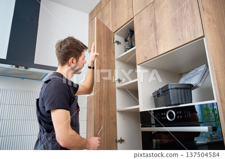 Man adjusting kitchen cabinet door with screwdriver at home Man adjusting kitchen cabinet door with screwdriver at home 137504584